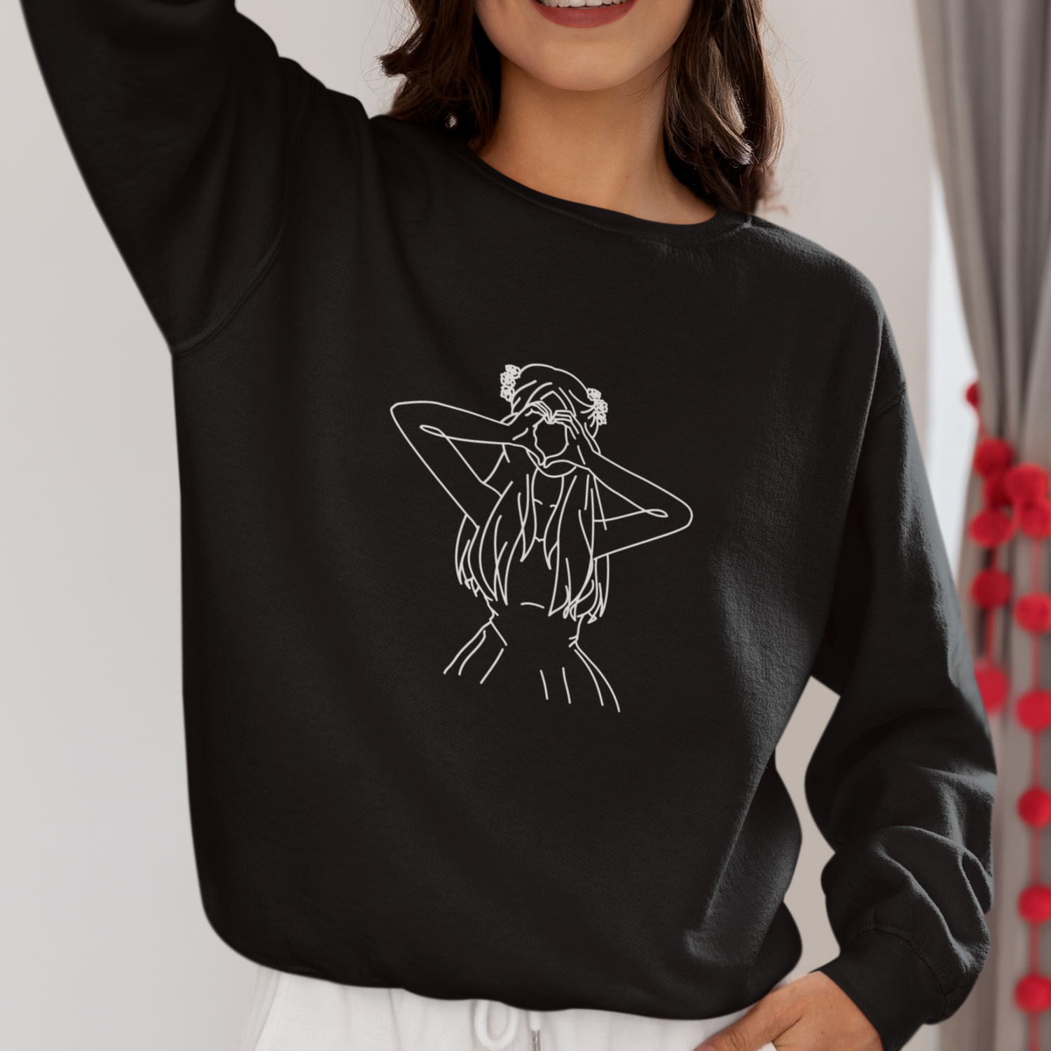 Woman with brown hair wearing a black sweatshirt featuring a delicate white line drawing of a woman making a heart with her hands, embodying the coquette and soft girl aesthetic.